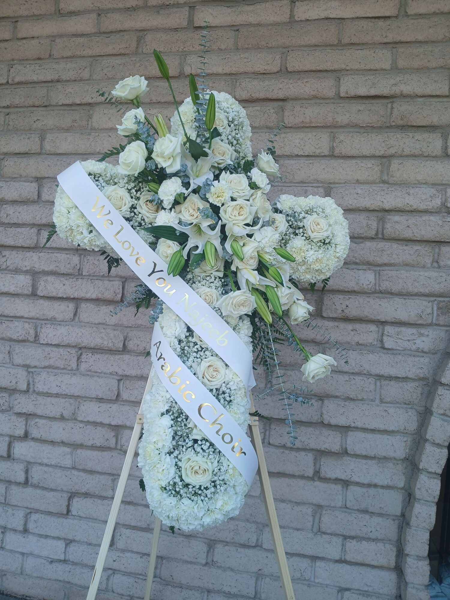 White floral arrangement with green leaves on a stand against a brick wall.