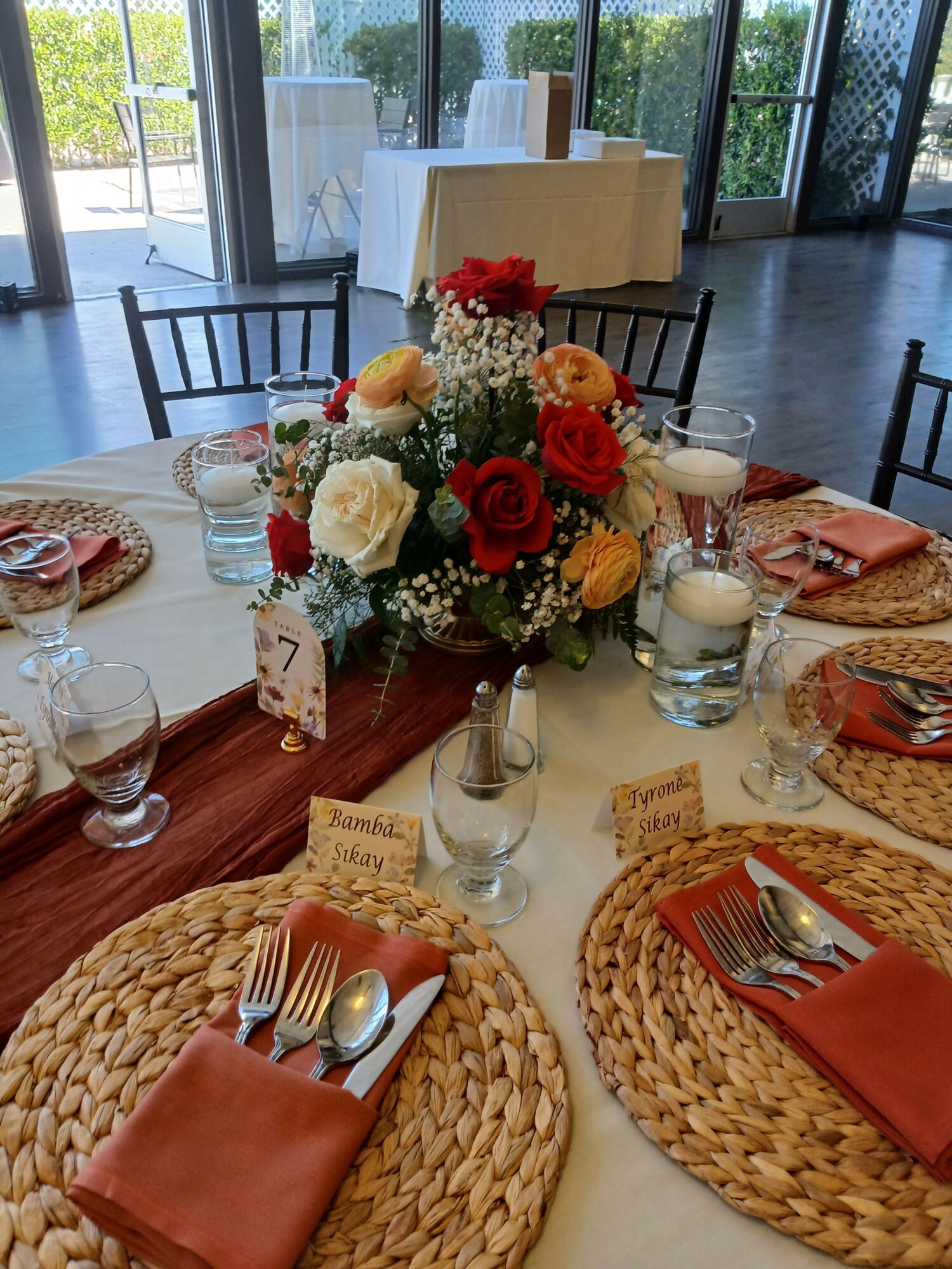 Table with floral centerpiece, glasses, plates, and napkins in a bright room with large windows.