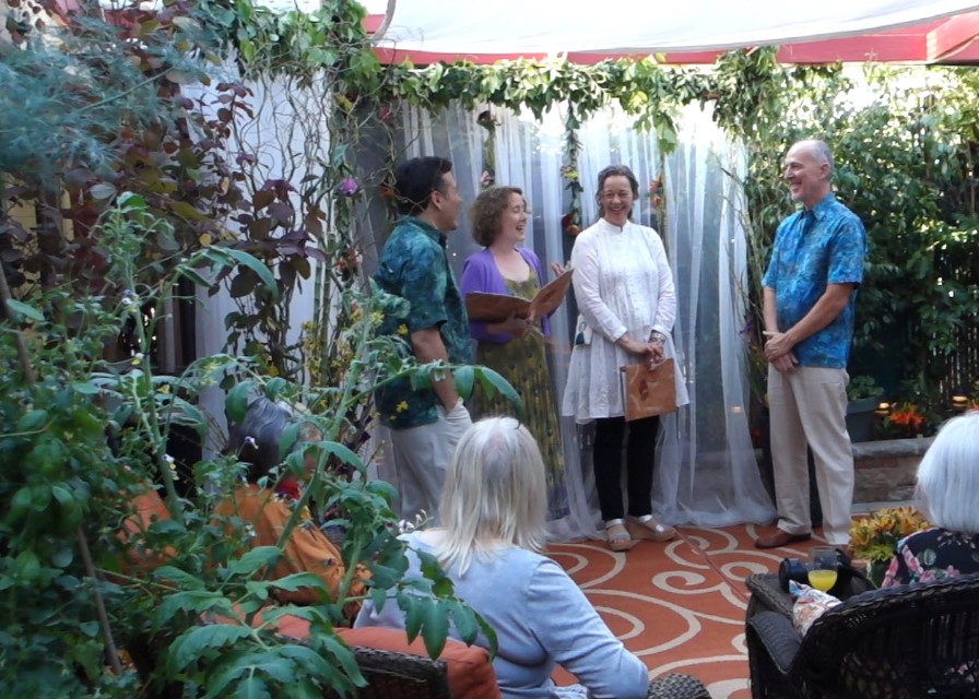 Group of five people standing outdoors, with three seated women in the foreground, surrounded by plants and greenery.