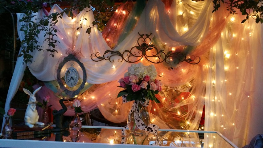 Decorative backdrop with draped fabric, string lights, a floral arrangement, and hanging ornaments.