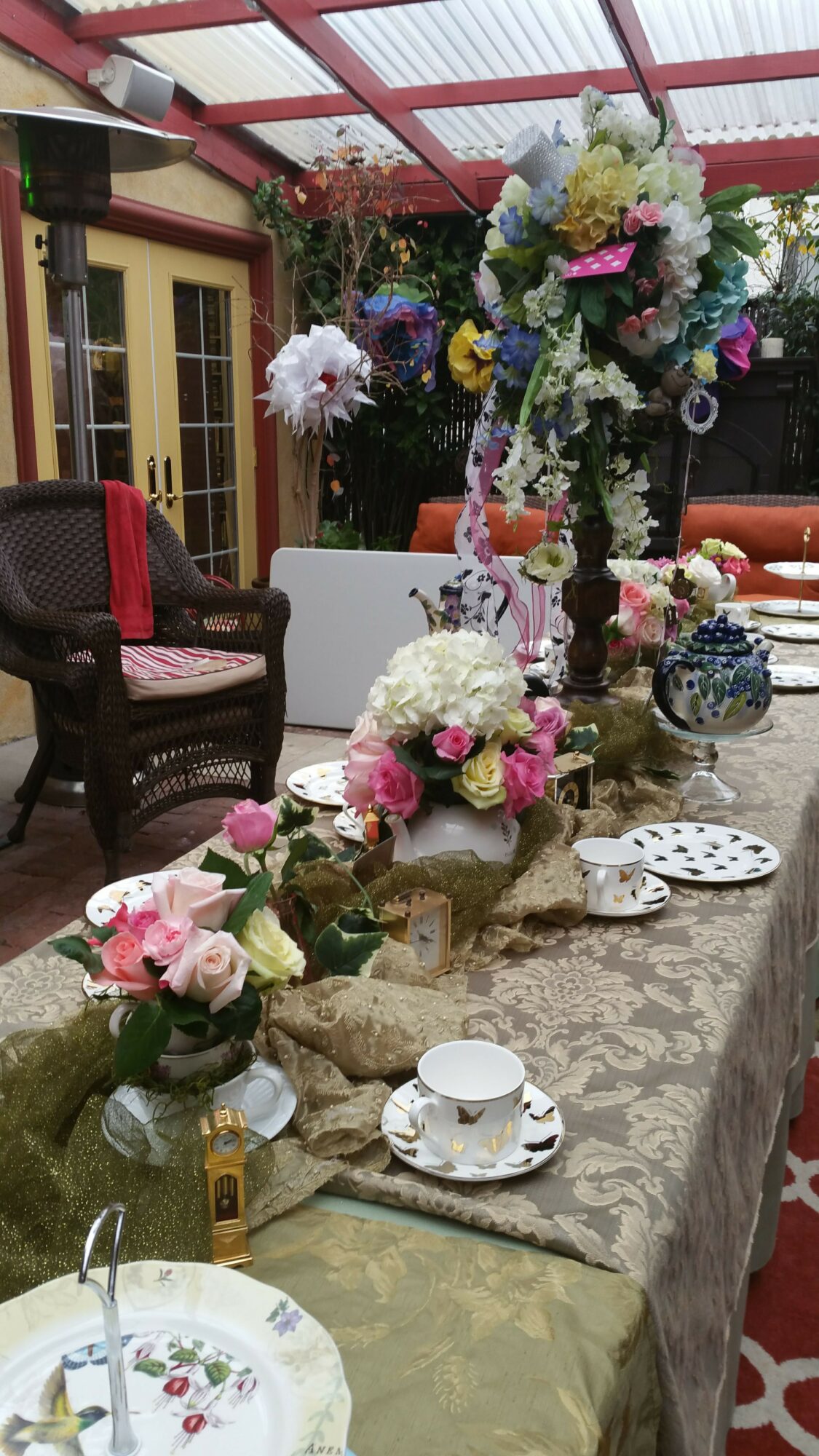 Table with floral arrangements, teacups, and decorative items in a decorated outdoor setting.