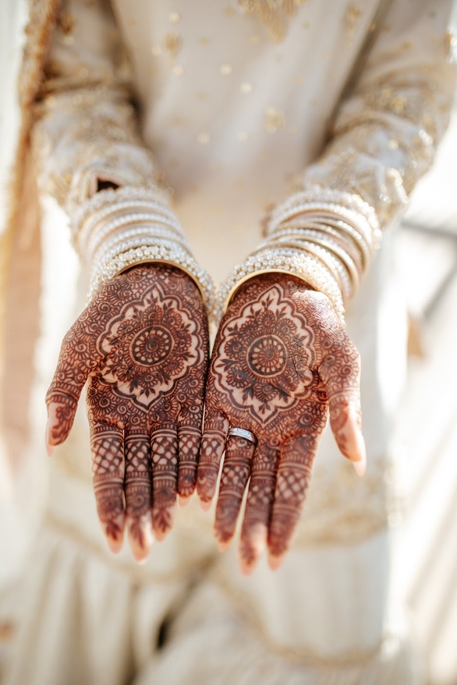 Person with intricate henna designs on hands, wearing multiple bangles and traditional attire.