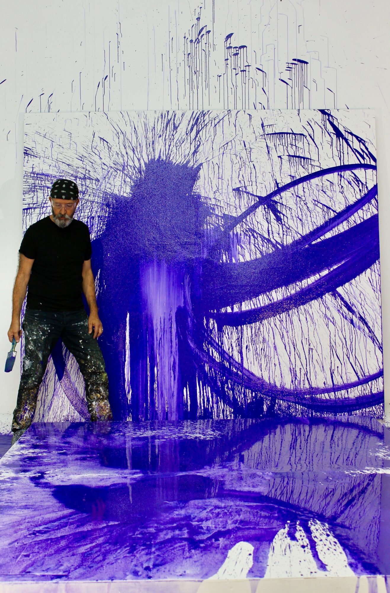 Person standing next to a large abstract purple and blue paint splash on a wall and floor.