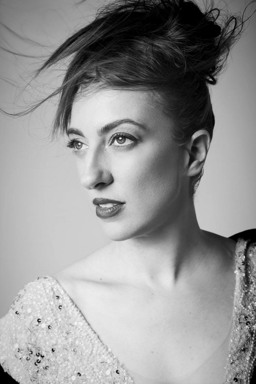 Black and white portrait of a woman with styled hair and a sparkly top, looking to the side.