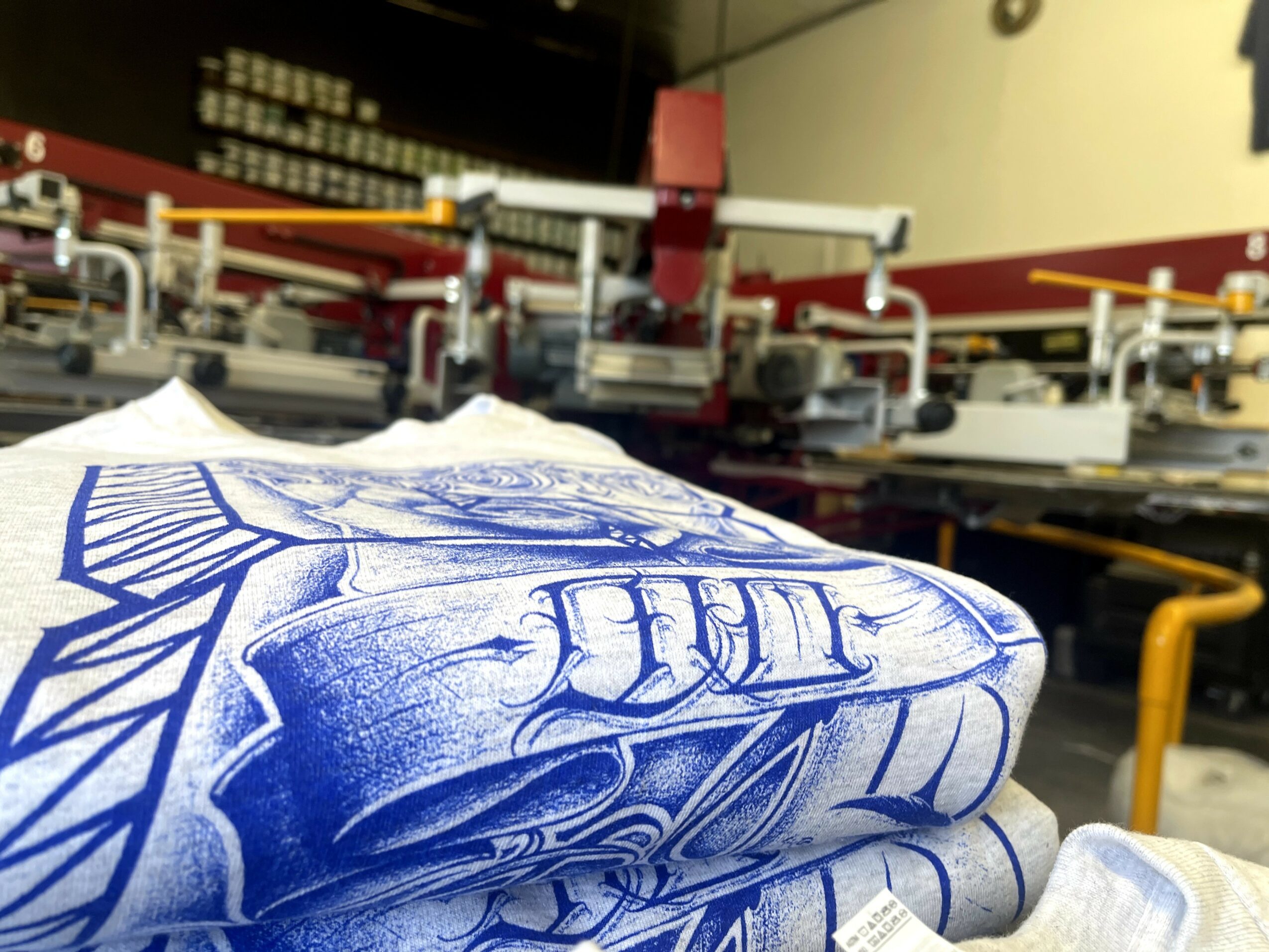Close-up of a detailed blue and white printed fabric with a design, in a workshop setting with machinery in the background.