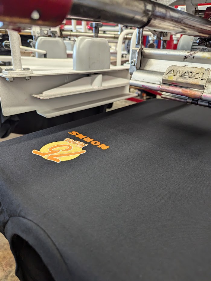 Close-up of a black fabric surface with orange and yellow text and logo, surrounded by metallic and plastic equipment parts.