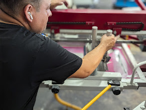 Person working with machinery in a workshop, wearing a black shirt, with tools and equipment around.