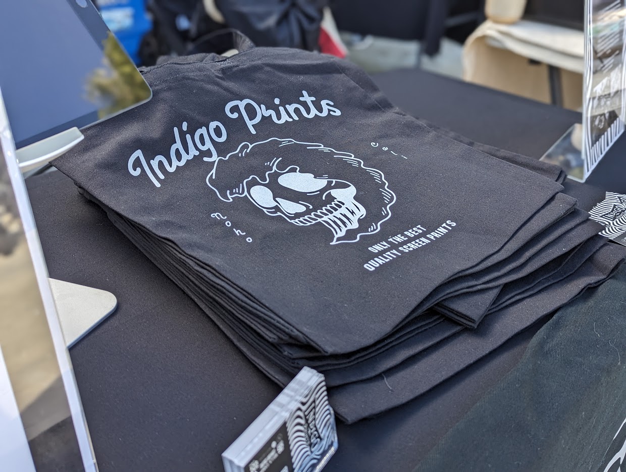 Stack of black tote bags with white logo and text on a table.
