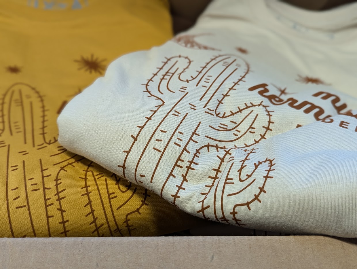 Two folded shirts with cactus designs, one yellow and one white, on a surface.