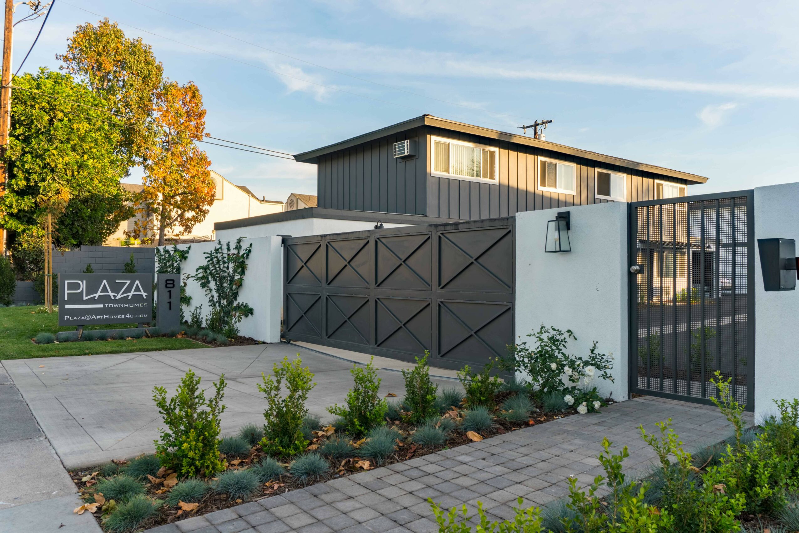 Modern building with a gray exterior, black gate, and landscaped garden with small bushes and plants.