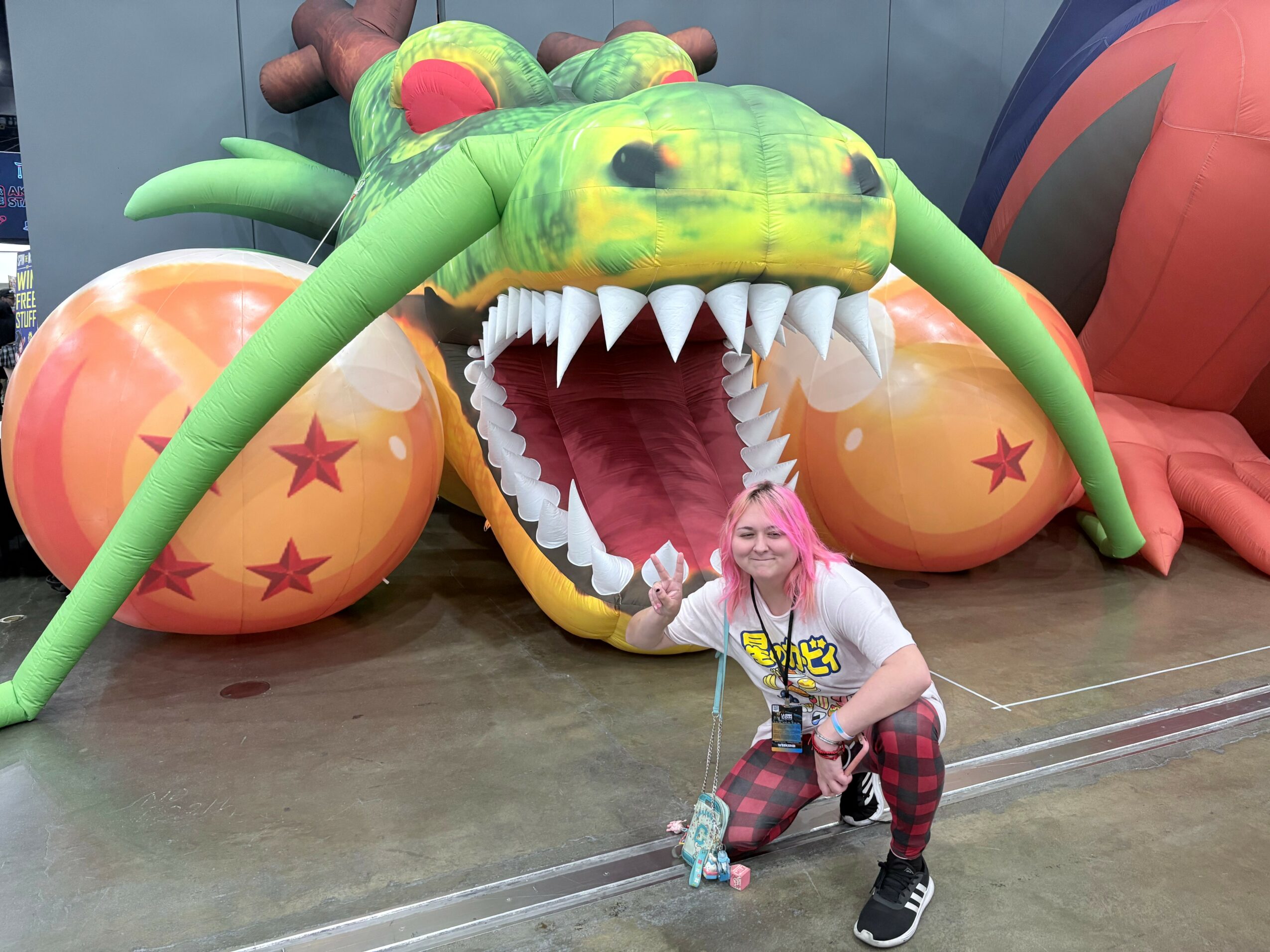 Child with pink hair crouching in front of a large dragon and balloon display, smiling outdoors.