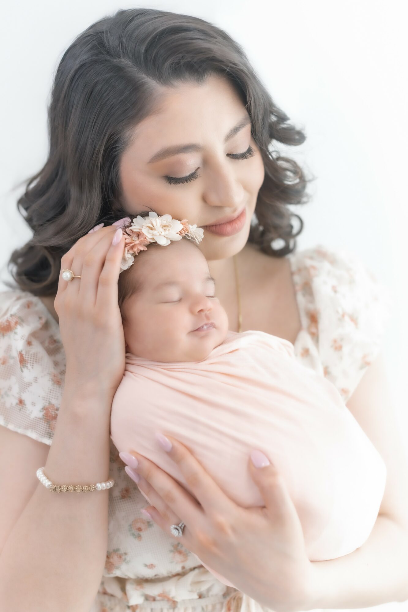 Woman holding sleeping baby with floral headband, close-up portrait, soft background.
