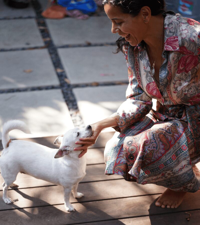 Woman crouching and petting a small white goat outdoors on a wooden surface.