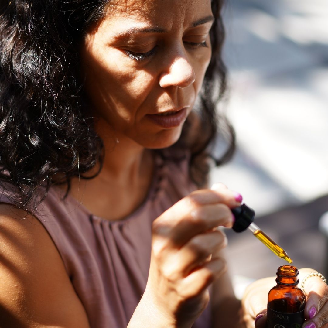 Woman with curly hair using a dropper to transfer liquid into a small bottle.