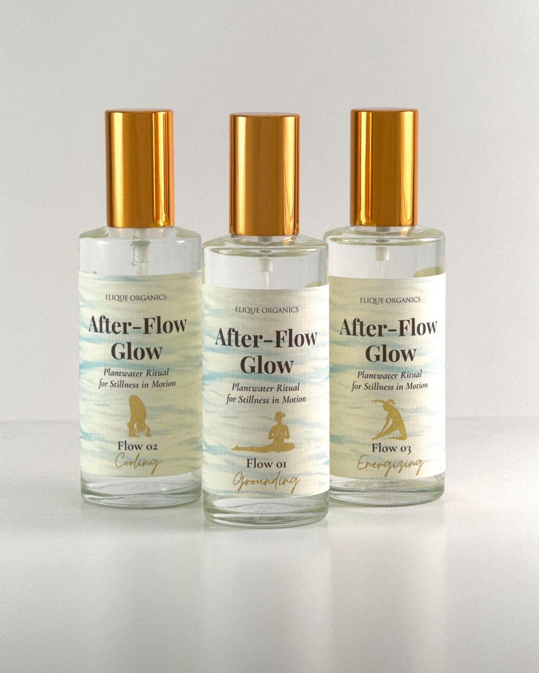 Three small bottles with gold caps labeled 'After-Flow Glow' and a gold logo, arranged in a row on a white surface.