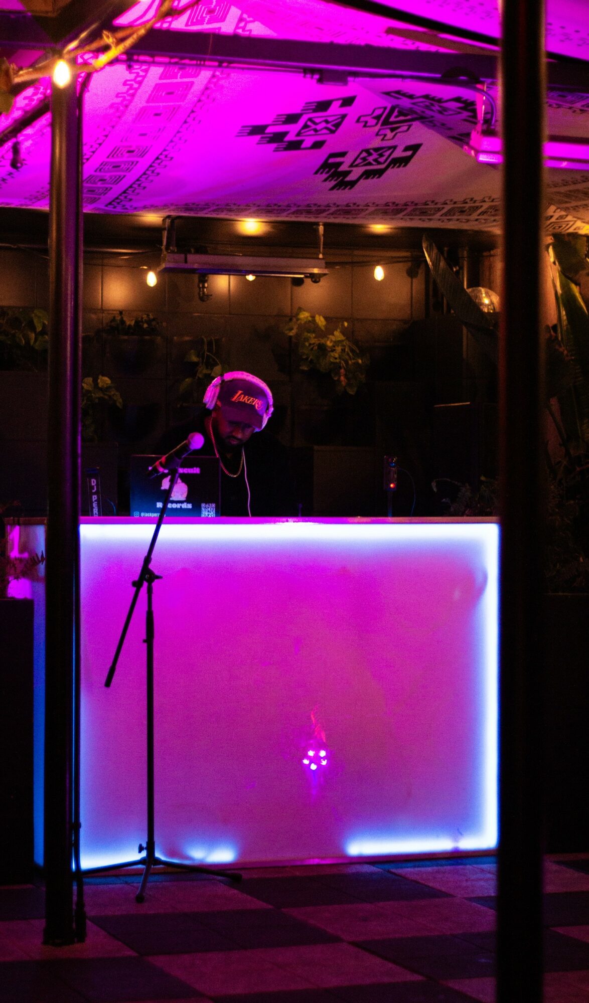 A DJ booth with colorful neon lighting, microphone stand, and a person behind the booth at night.