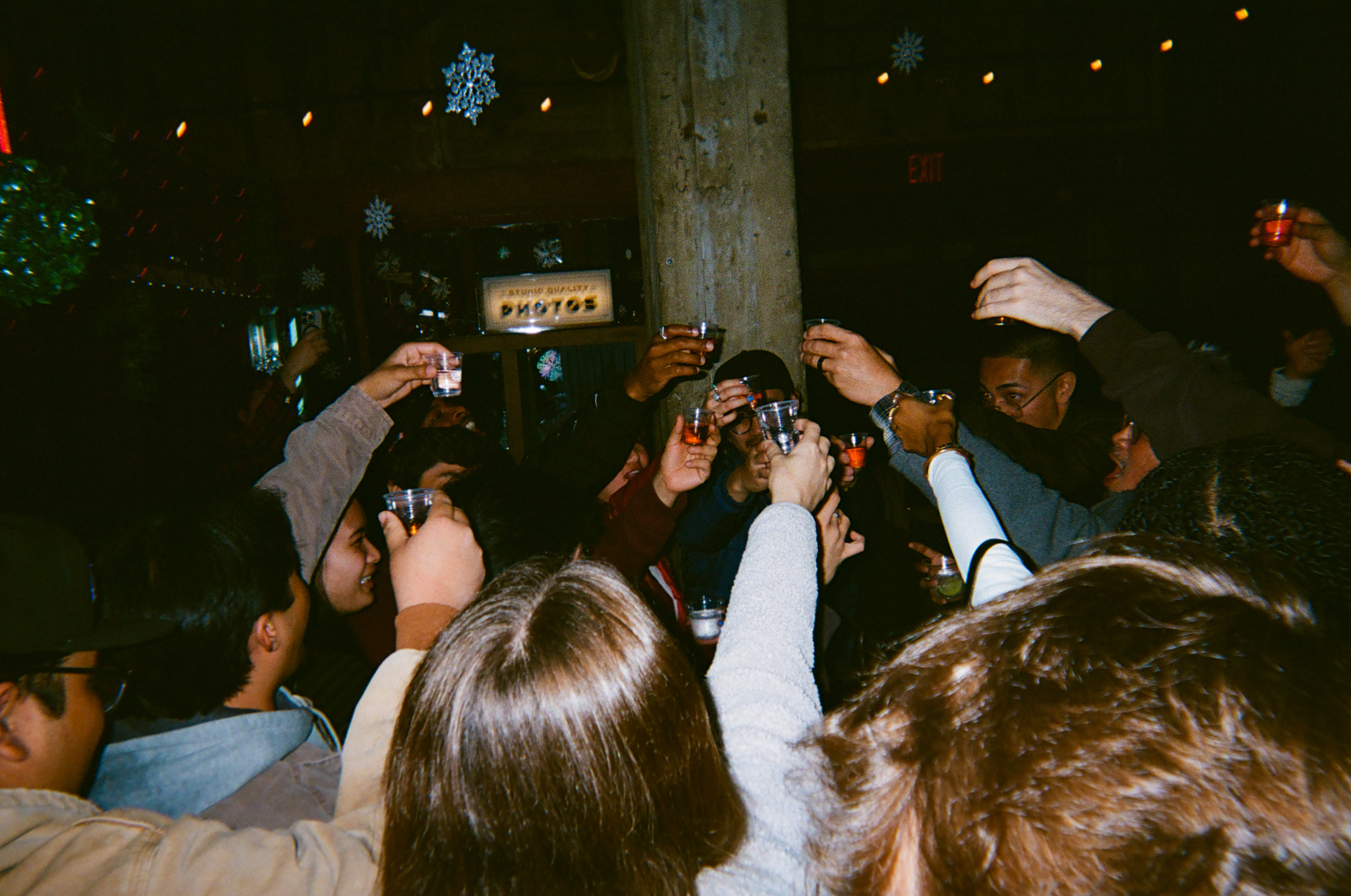 Group of people raising glasses outdoors at night, celebrating around a tree with festive decorations.