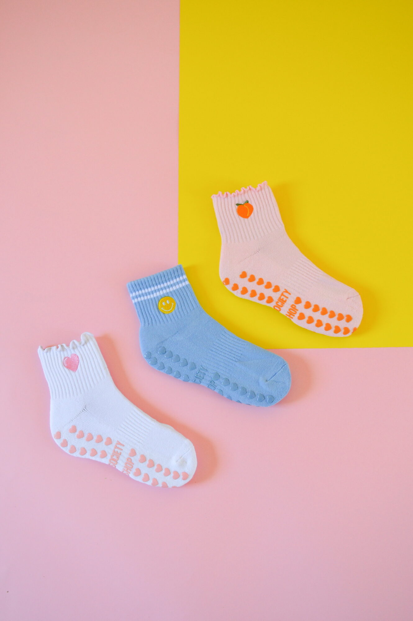 Three colorful socks with heart and dot patterns on pink and yellow background.