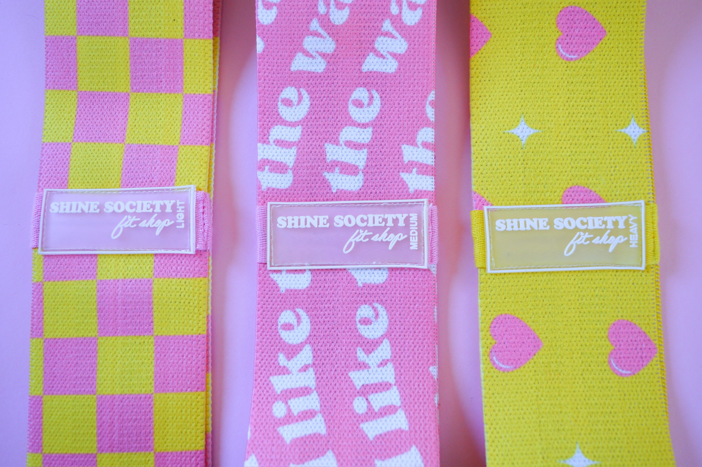 Three colorful fabric wristbands with labels, pink, yellow, and checkered patterns, arranged vertically.