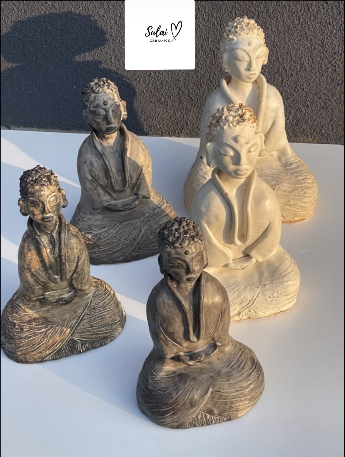 Six small Buddha statues with different poses and finishes, arranged on a white surface against a dark background.