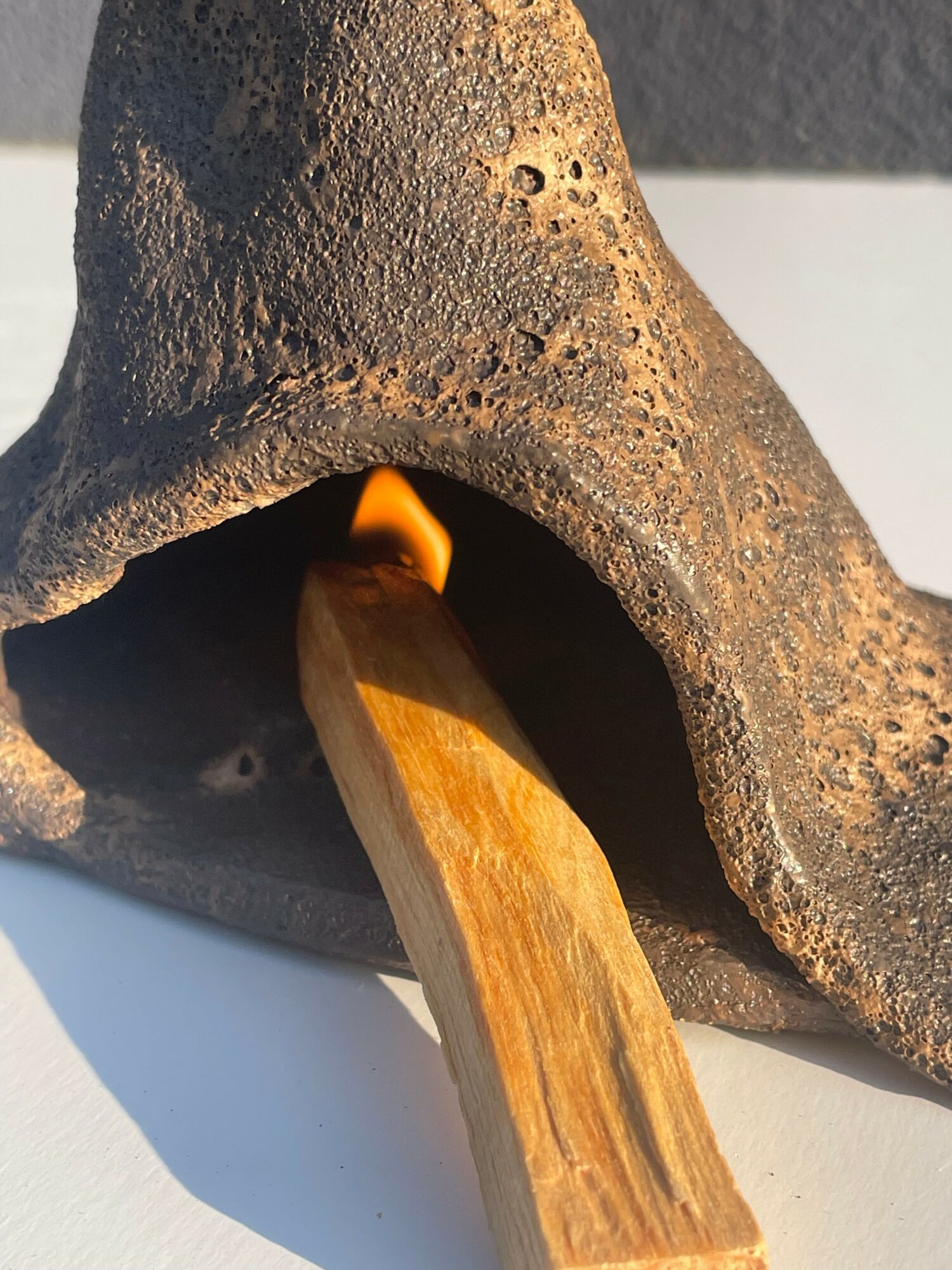 Wooden stick inserted into a small opening of a textured, dark, cone-shaped object with a flame at the tip.