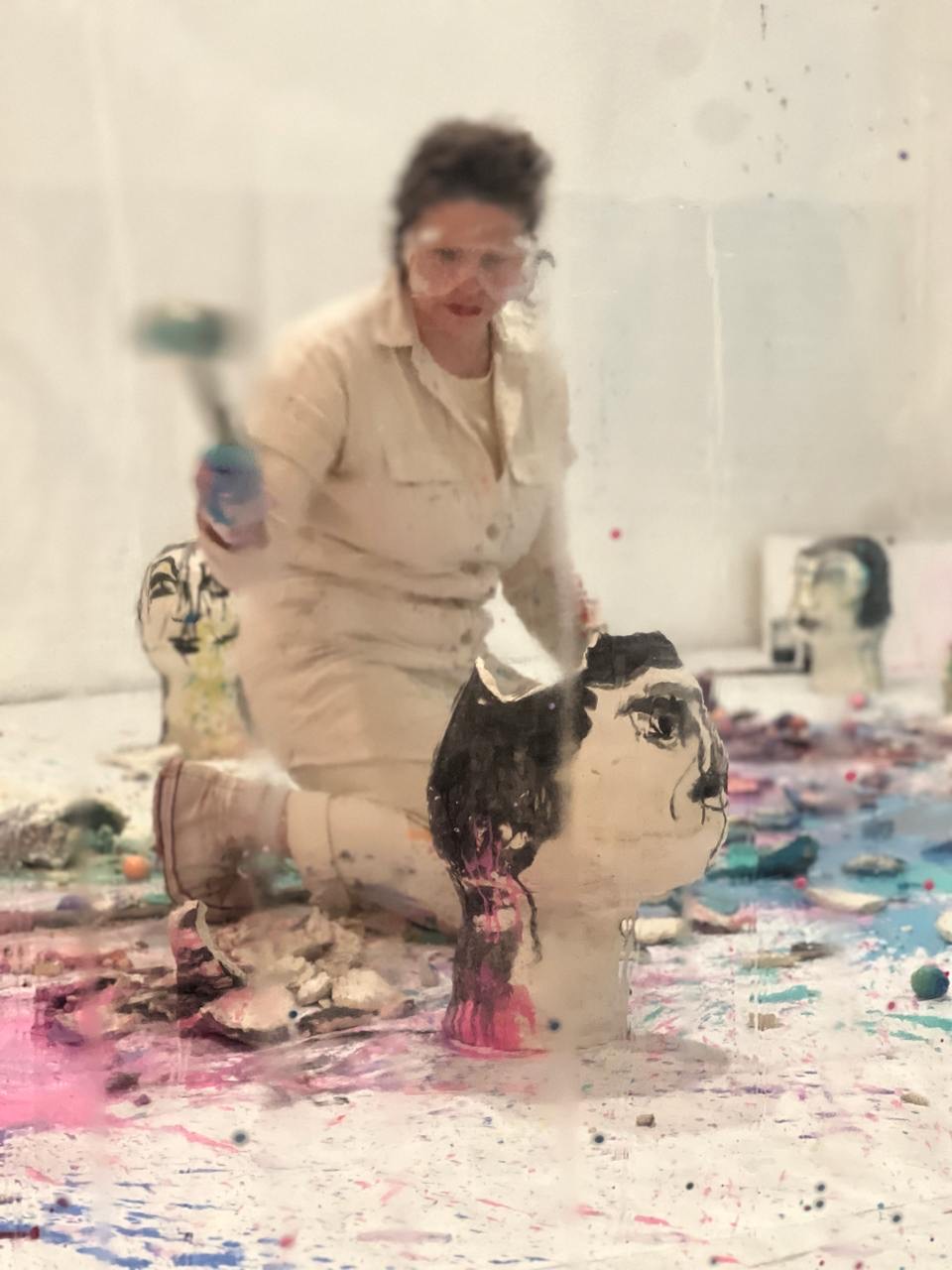 Person working on large head sculptures with paint and tools in a studio.