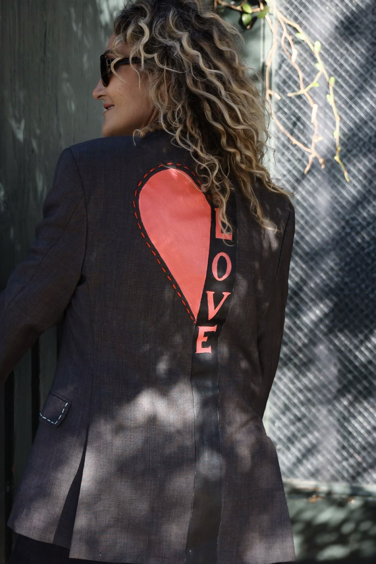 Woman with curly hair wearing a black blazer with a red heart and the word 'LOVE' on the back.