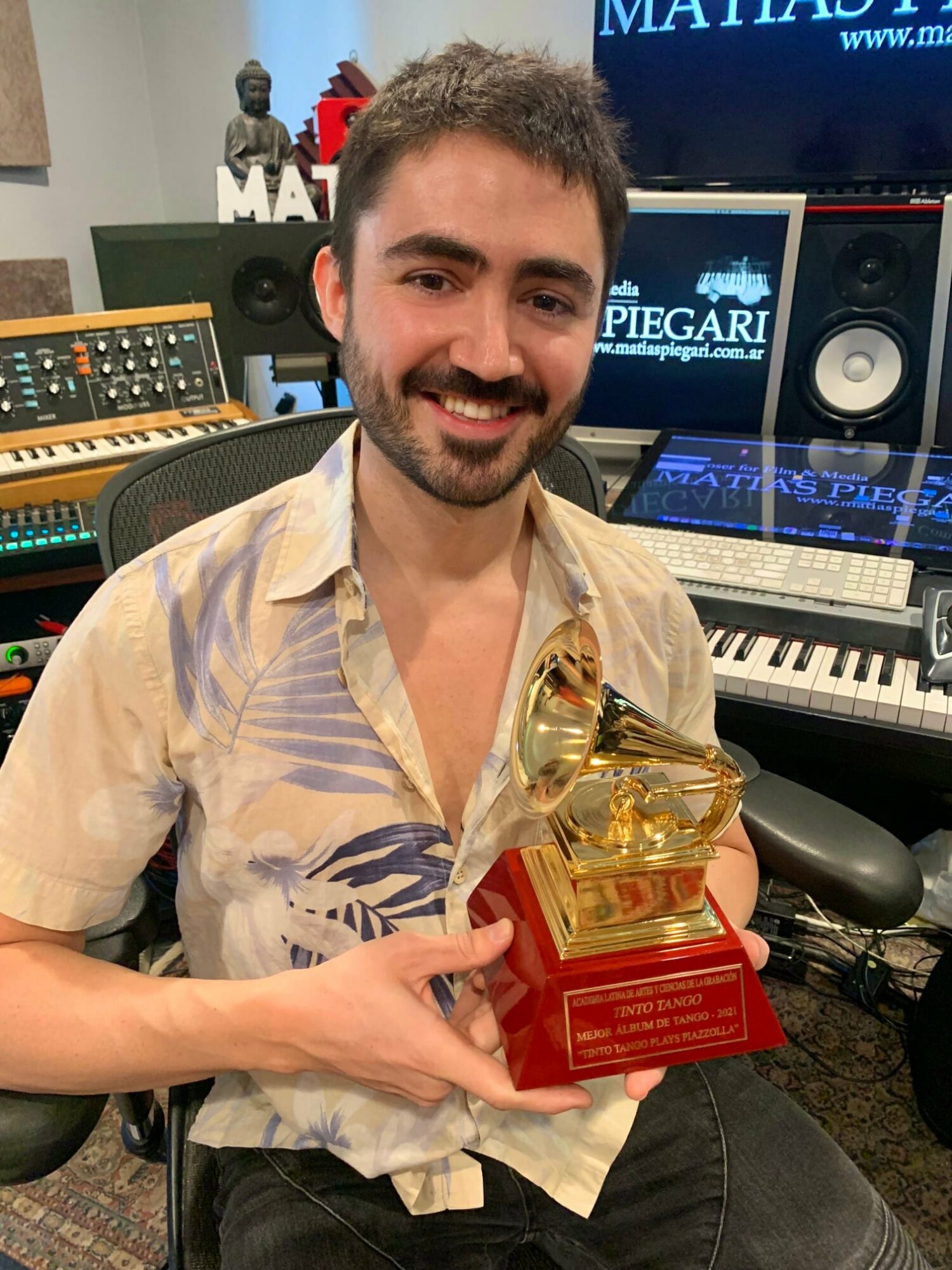 Man with dark hair and beard holding a gramophone trophy in a music studio.