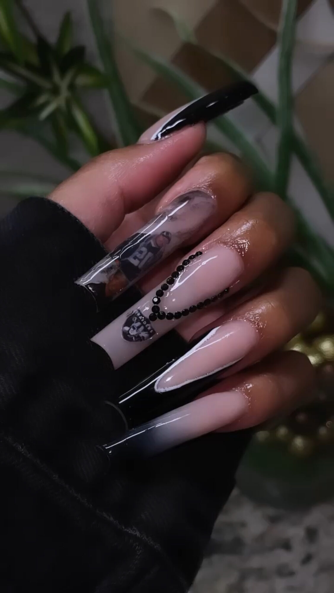 Hand with long, decorated nails, some with black and white designs, holding a transparent phone case.