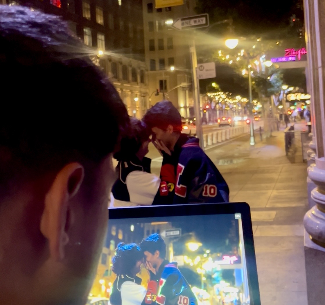 Person holding tablet captures a photo of two children on city street at night, illuminated by streetlights and buildings.