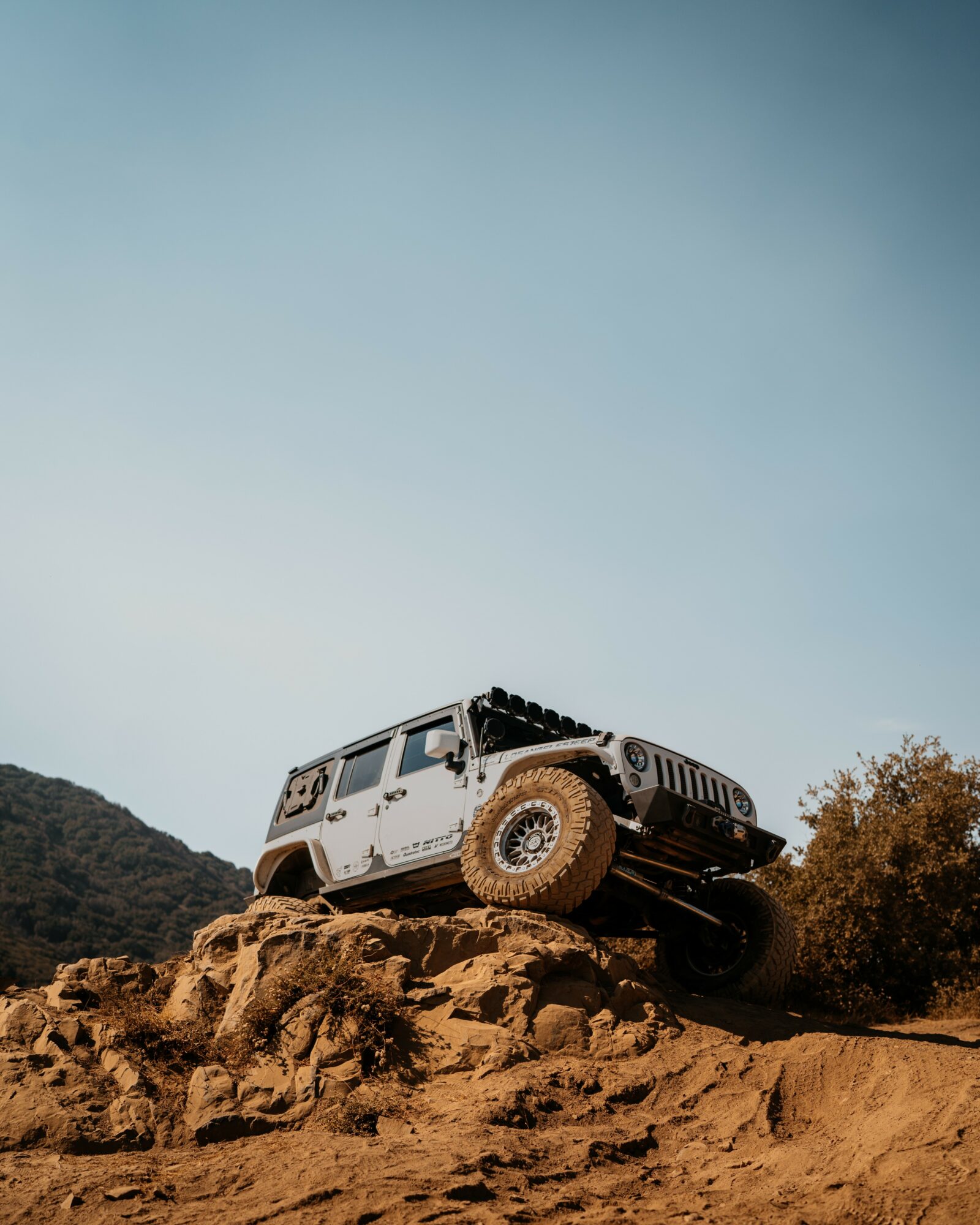 Off-road vehicle on rocky terrain with a clear sky and distant hills in the background.