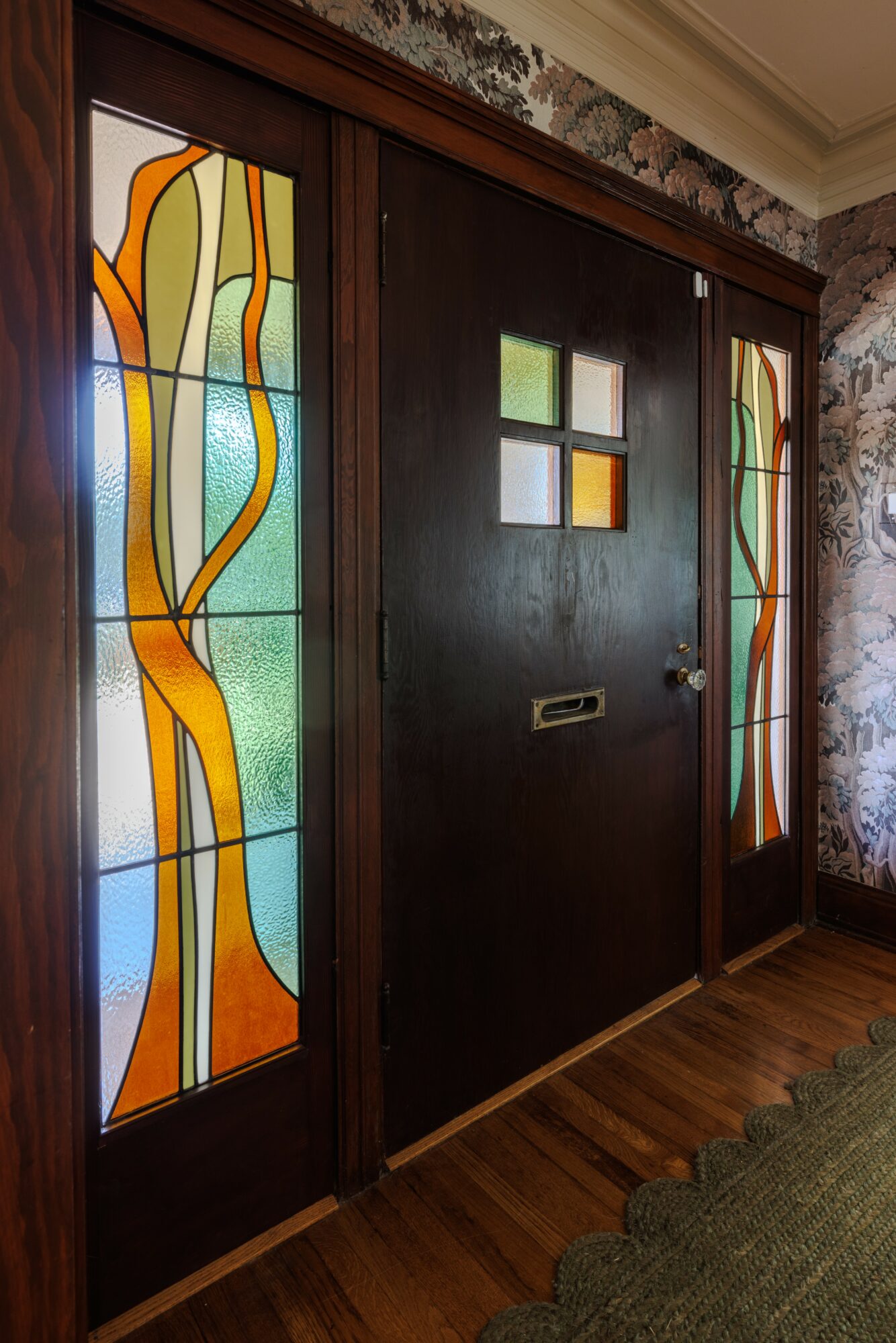 Wooden door with four small square windows and stained glass panels on sides, in a room with brick wall and wooden floor.