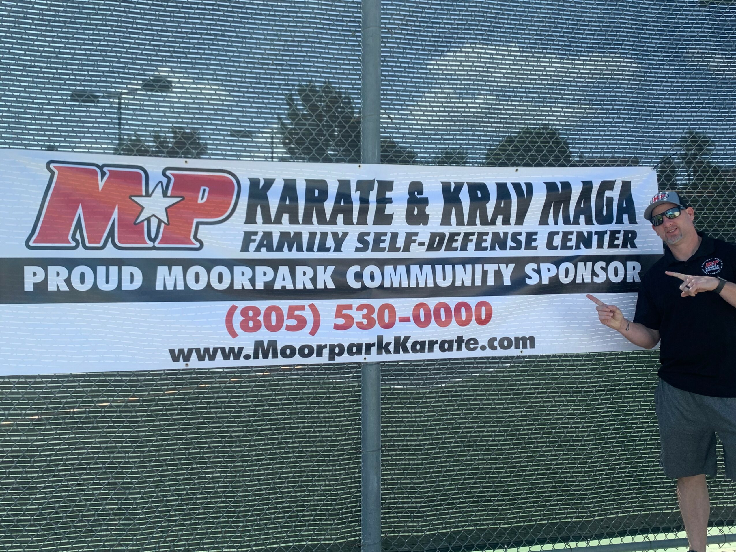 Man standing next to a large banner for a karate and Krav Maga family self-defense center.