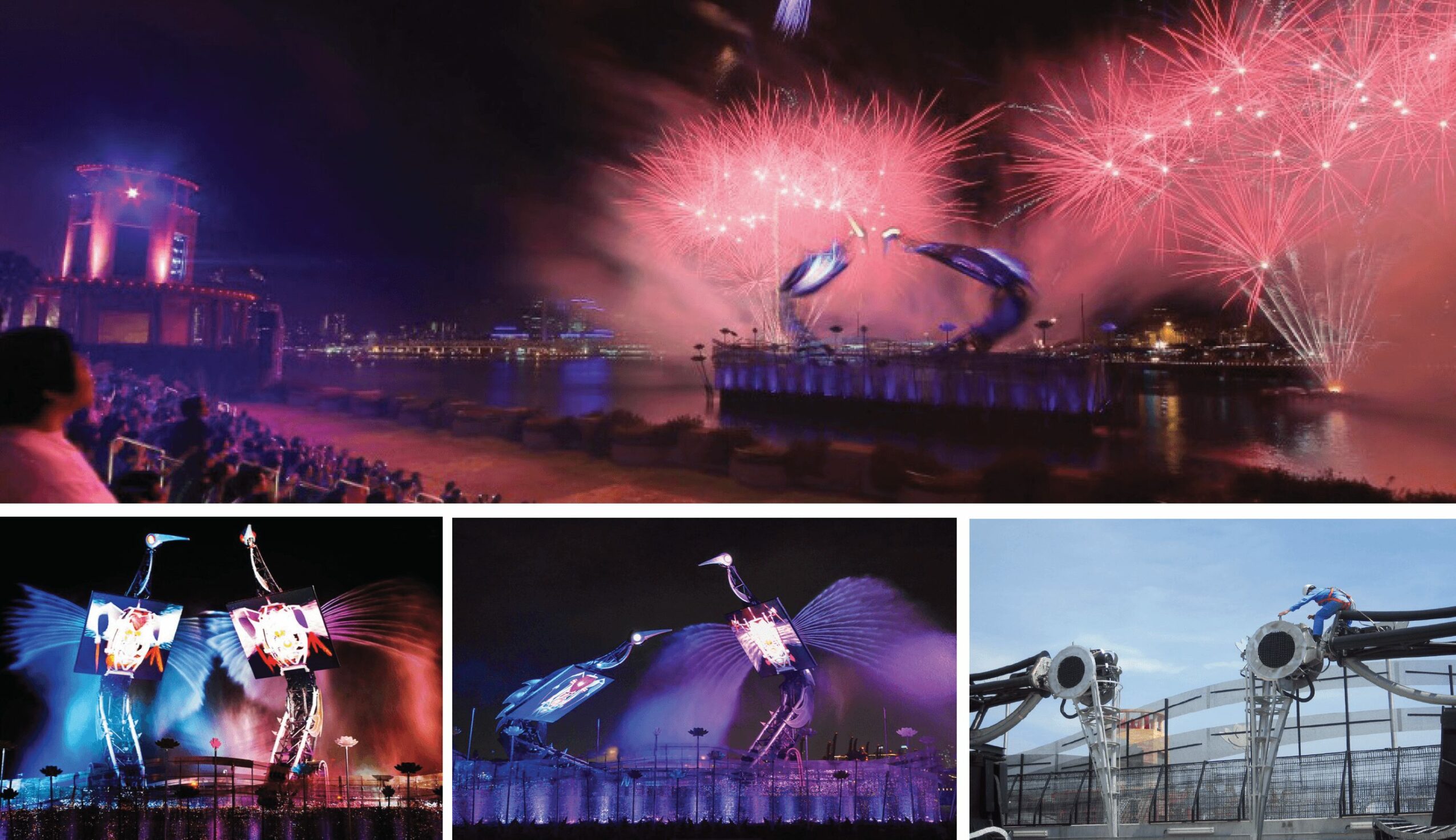 Fireworks display over water with reflections, crowd watching, and a large illuminated structure in the background.
