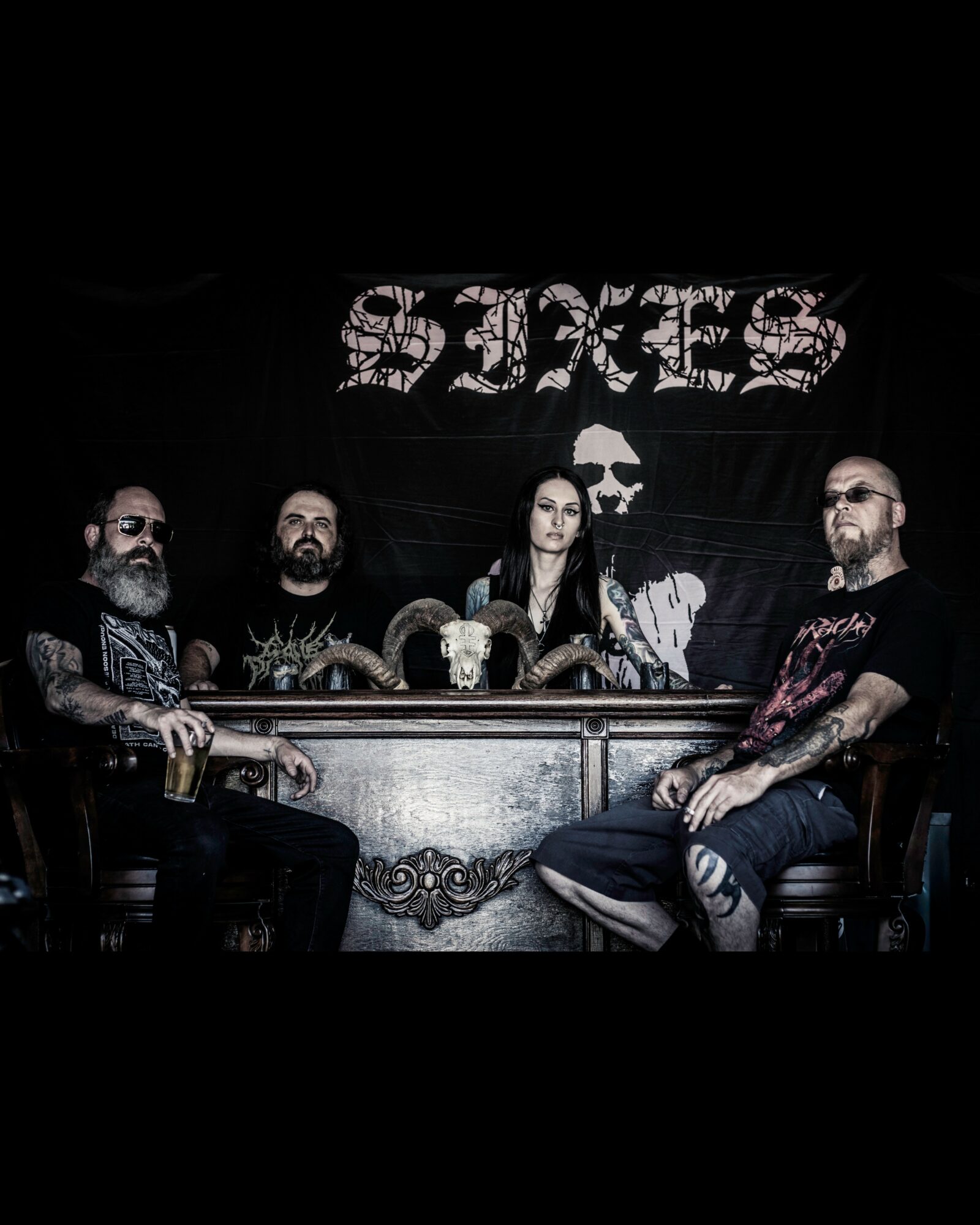 Four people sit at a bar with a large black and white banner behind them reading 'SIXES'.