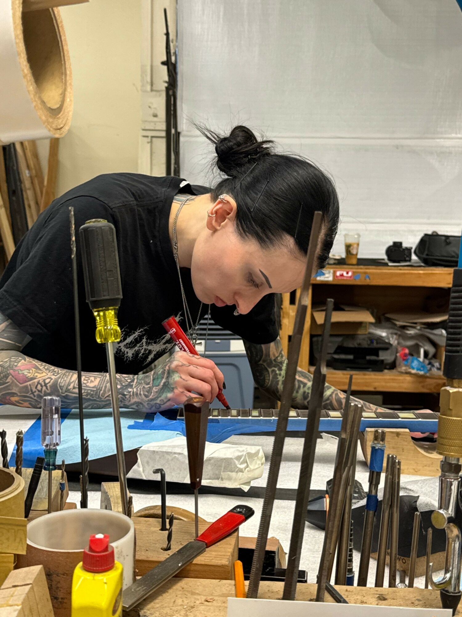 Person working on a craft project at a cluttered workspace with tools and materials.