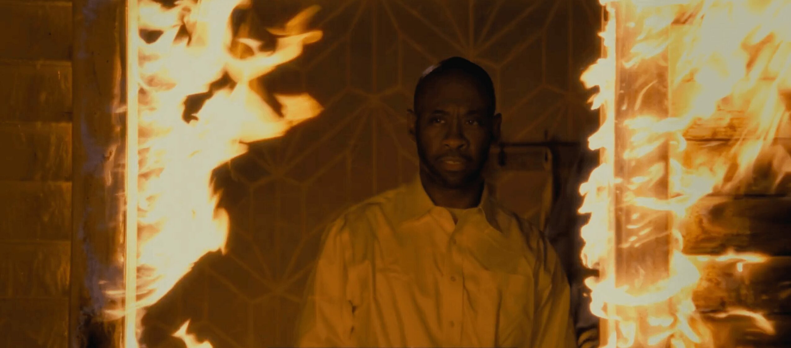 Man standing in front of a burning background with flames and geometric patterns.