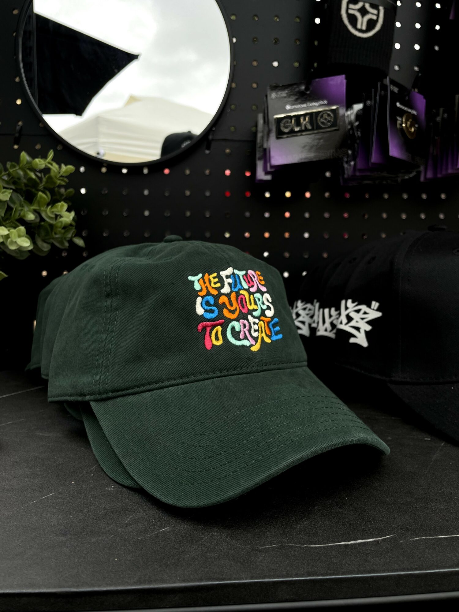 Dark green baseball cap with colorful embroidered text on front, placed on a black surface.