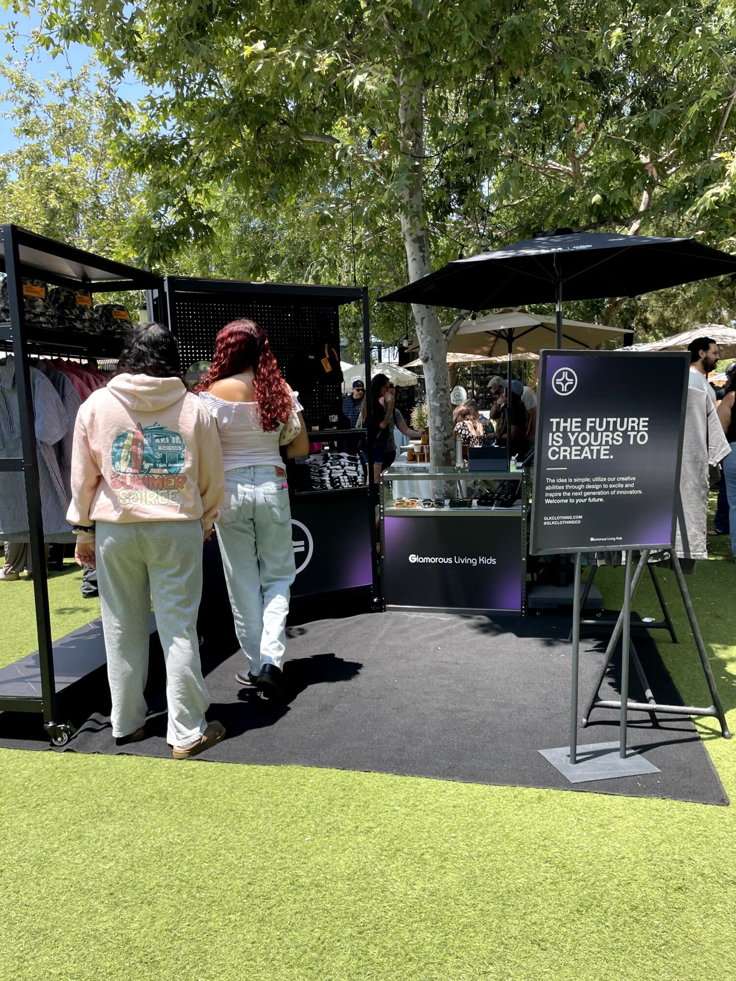 People gather around a booth with a sign about future technology and creativity outdoors under trees.