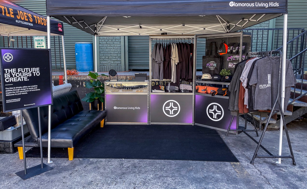 Outdoor booth with clothing displays, a black sofa, and a sign about creating the future, under a canopy.