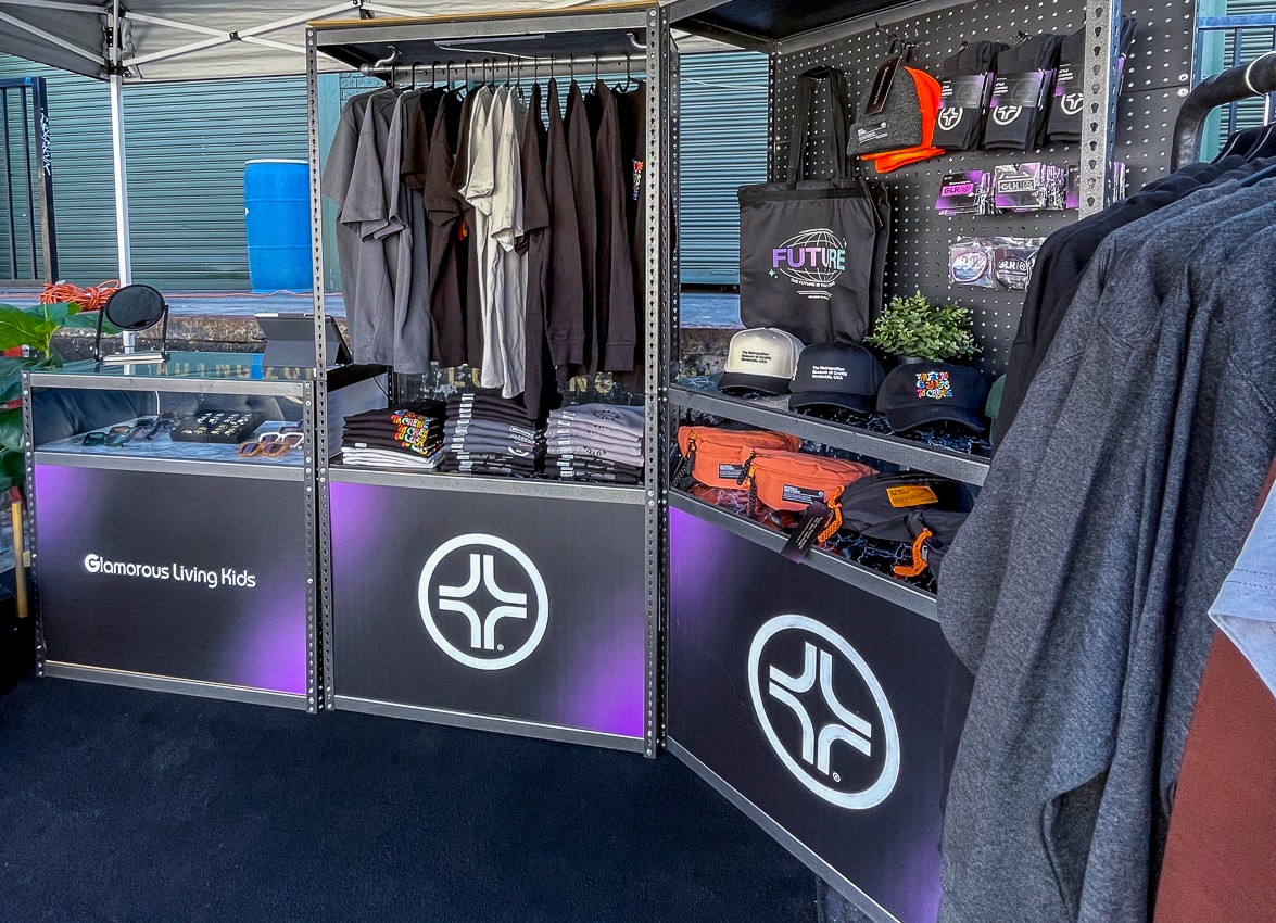 Display booth with clothing, bags, and outdoor gear, including jackets, backpacks, and helmets, on shelves and racks.
