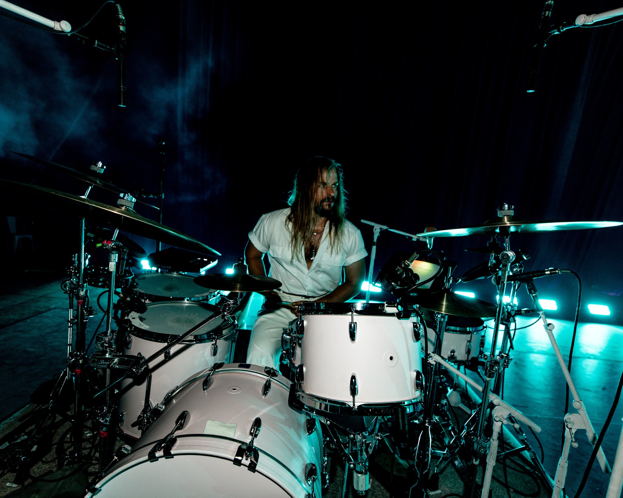 Person playing drums on stage with dark background and stage lights.