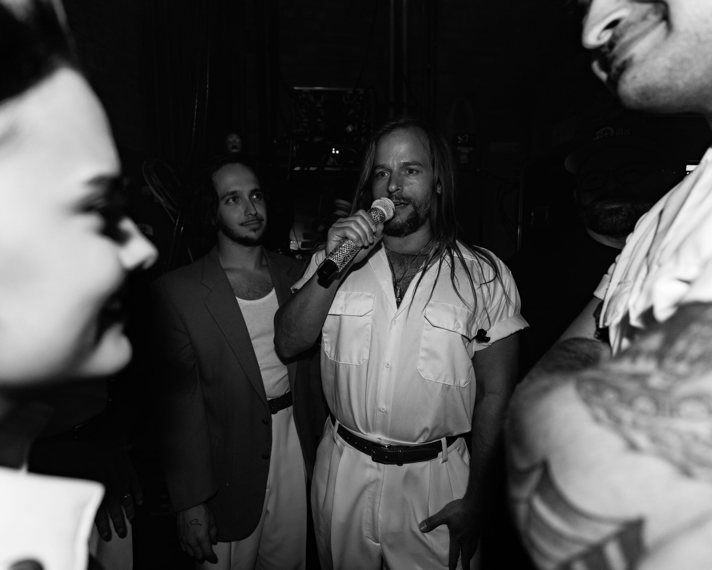 Group of people, one person speaking into a microphone, others listening, in a dark setting.