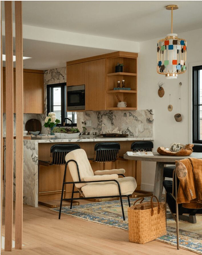 Living room with wooden cabinets, marble backsplash, black chairs, beige armchair, and a colorful hanging lamp.