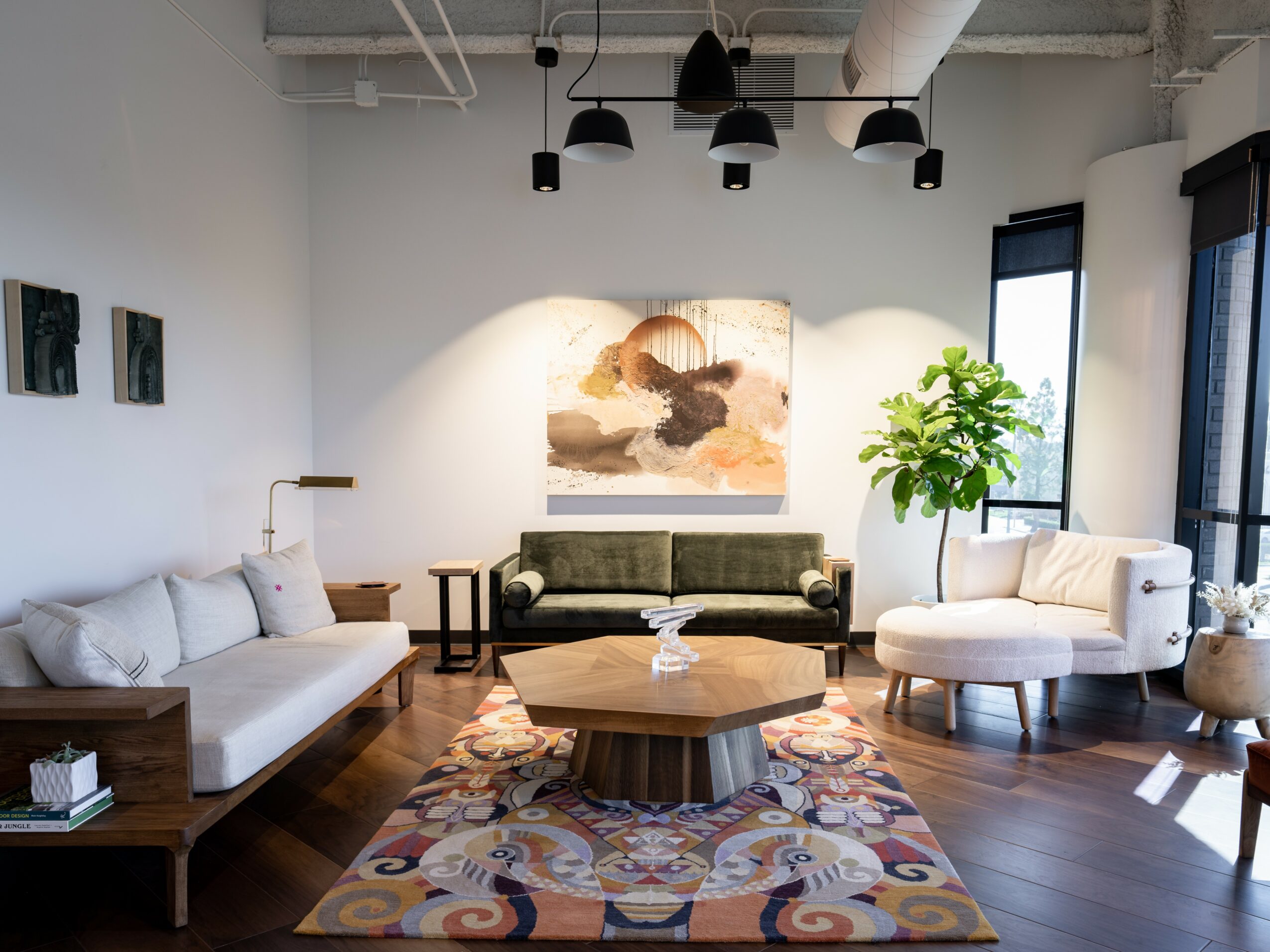 Living room with sofas, a coffee table, a colorful rug, and large windows with black blinds.