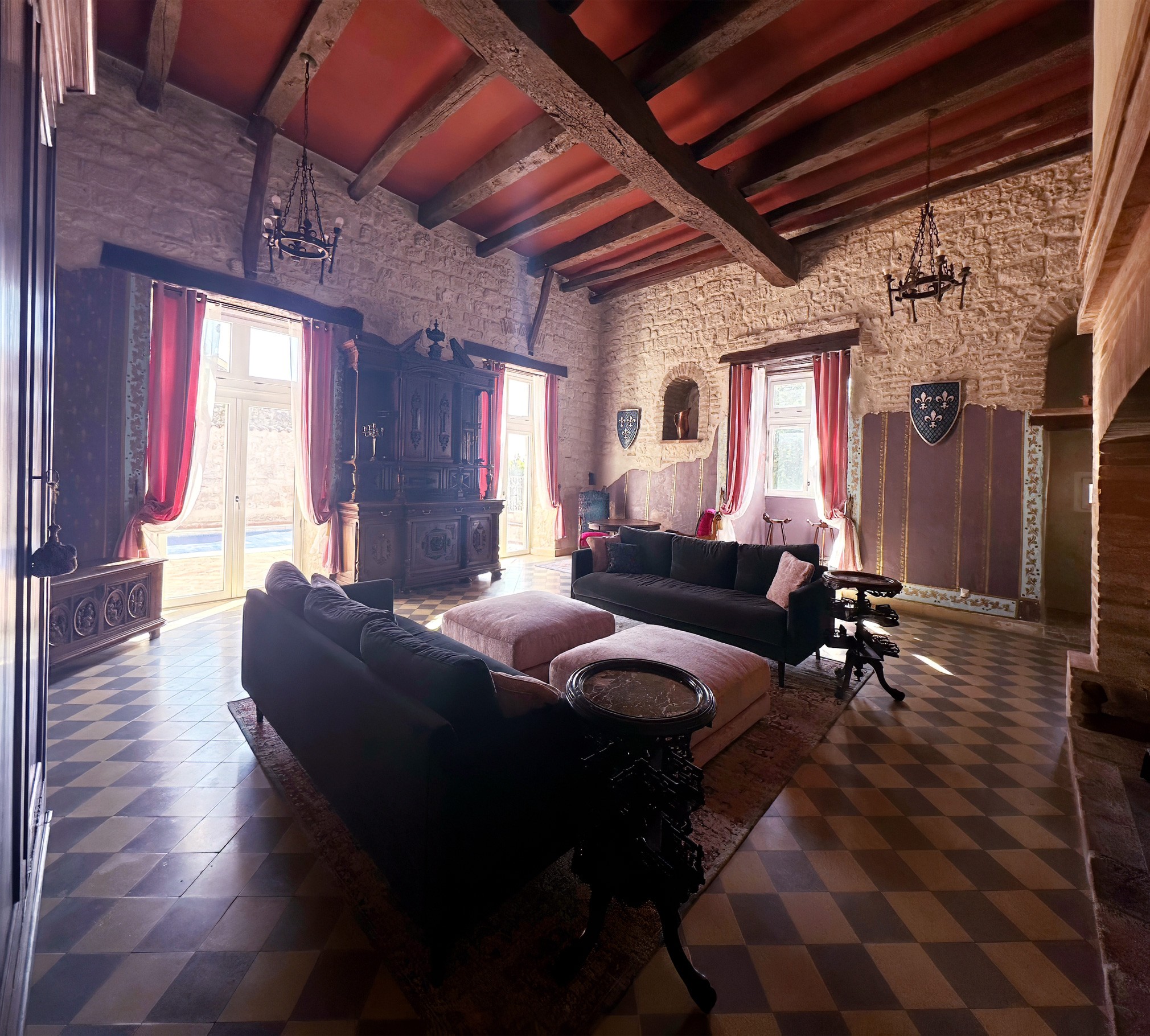 Interior of a historic room with wooden ceiling beams, stone walls, large windows with red curtains, and antique furniture.