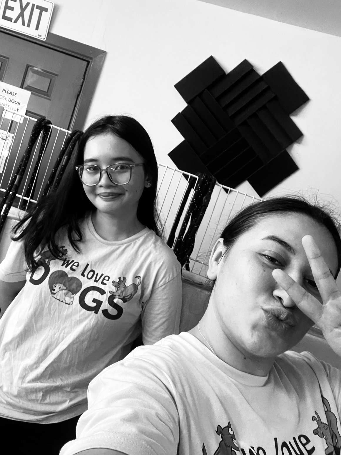 Two young women taking a selfie in a room with soundproofing foam on the wall and an exit door in the background.