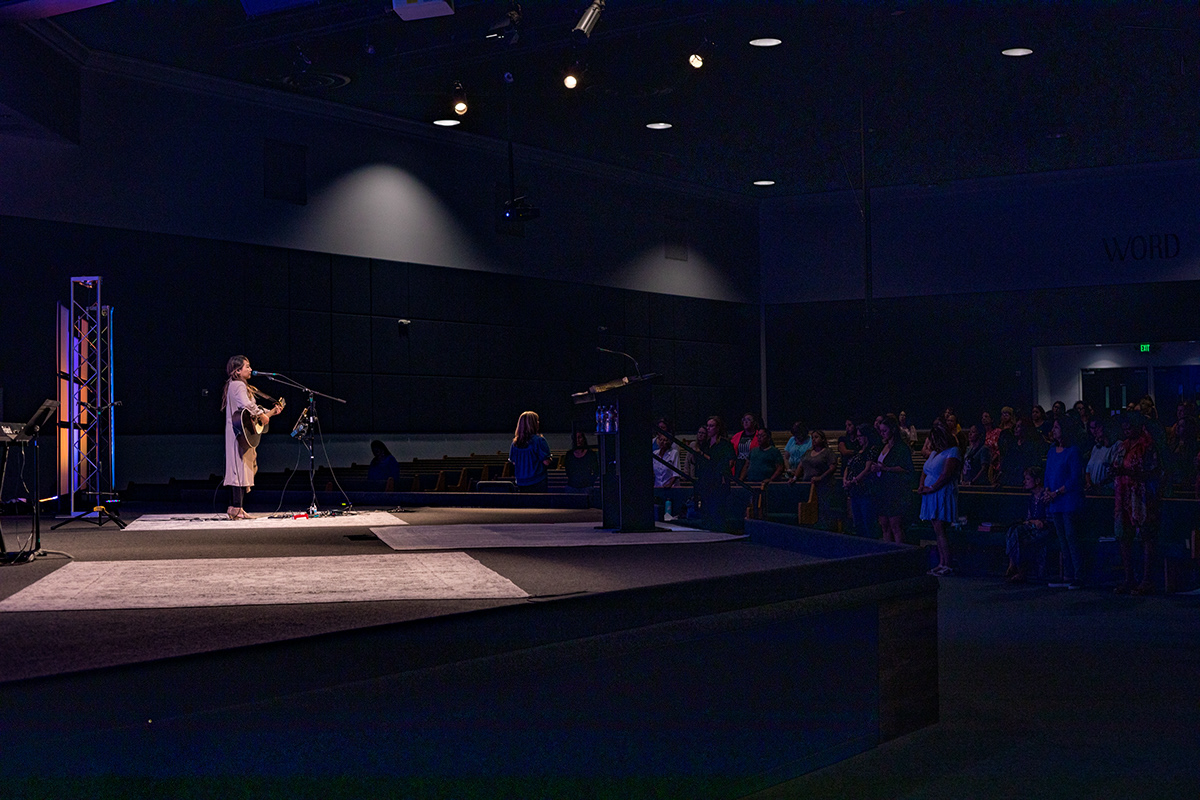 Person performing on stage with microphone in front of audience in dark auditorium.