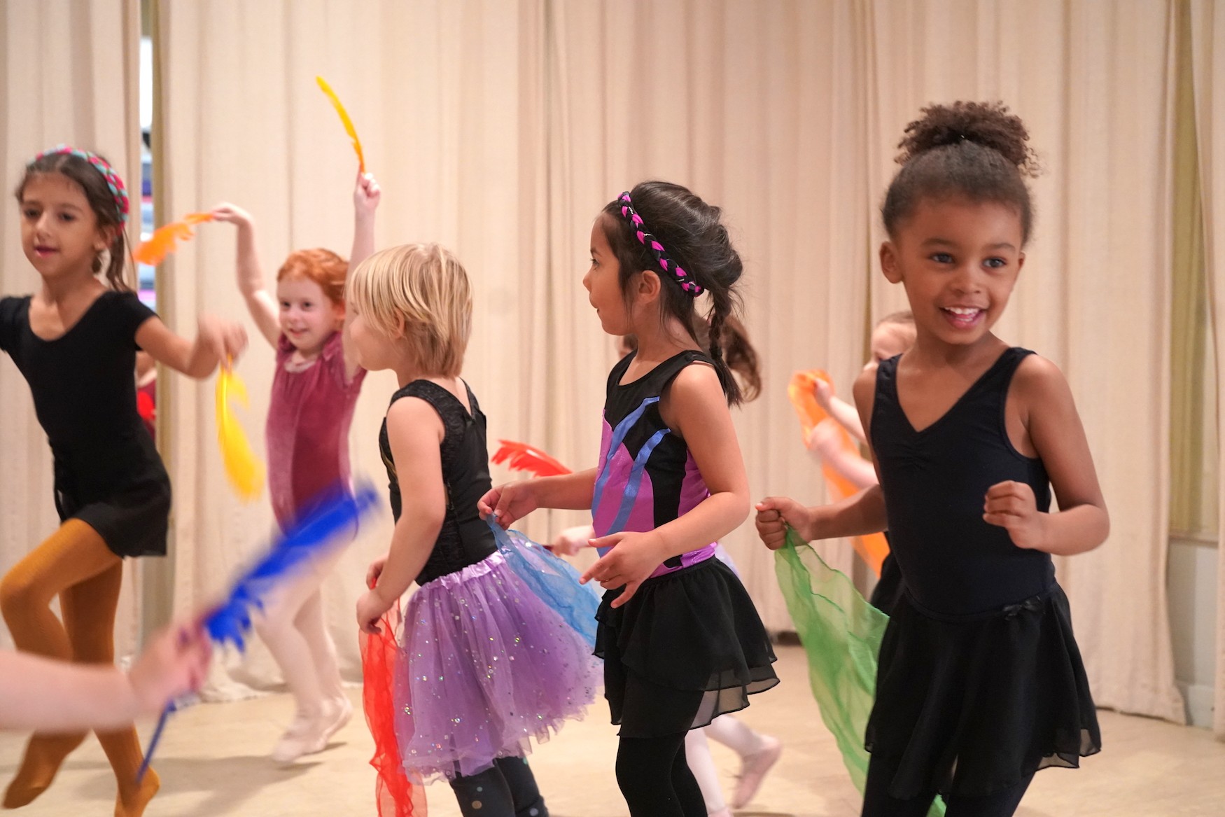 Group of children dancing and playing with colorful ribbons in a room with curtains.