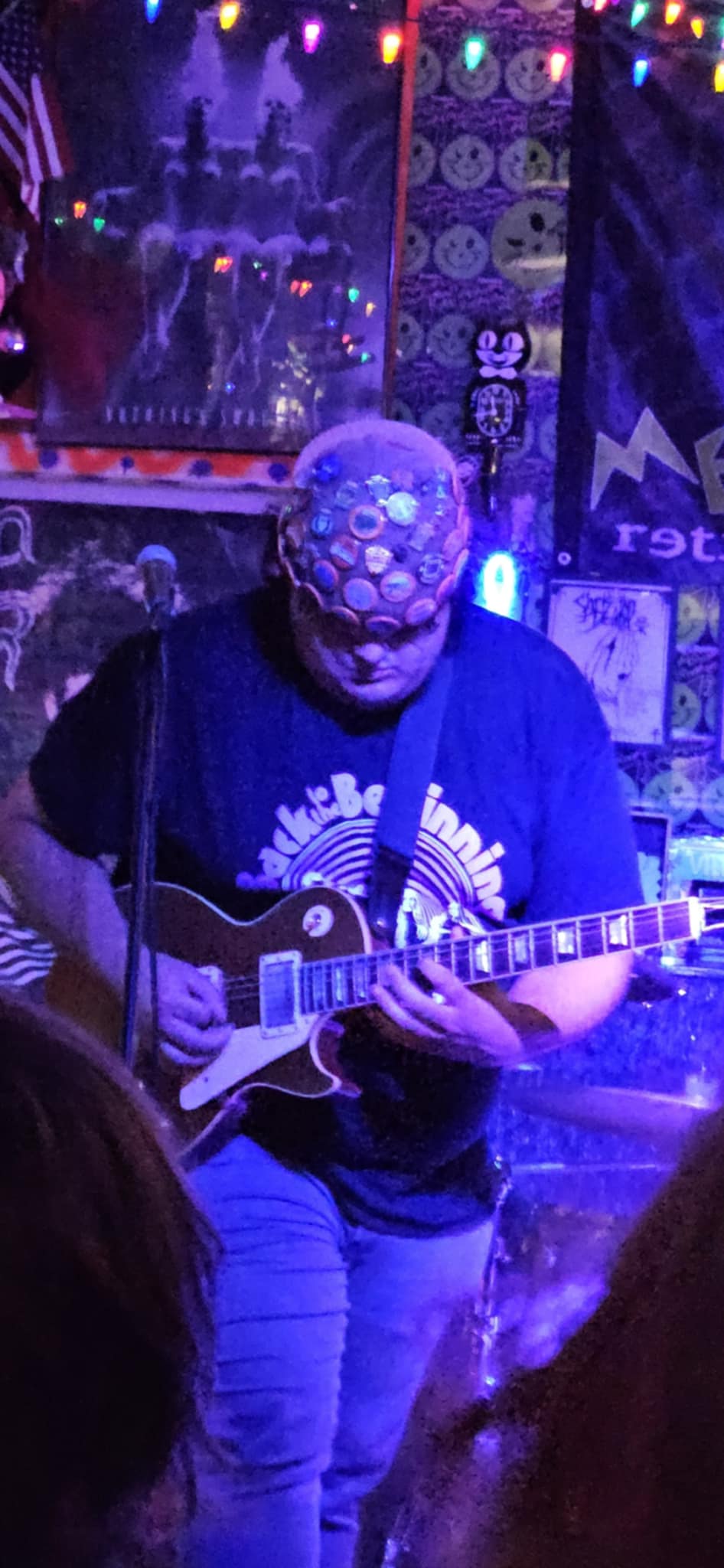 Person playing guitar on stage with colorful lights and decorations in background.